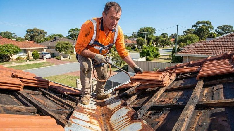 Professional roofer lifting tiles to inspect a deteriorating valley iron during a Perth roof assessment